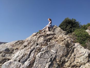 Low angle view of woman on rock against clear blue sky