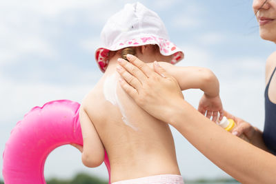 Mother applying suntan lotion on daughter against sky