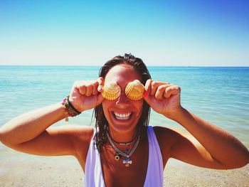 Close-up of cheerful young woman covering eyes with seashells at beach