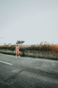 Woman on road amidst field against clear sky