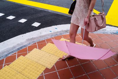 Low section of woman with shoulder bag and umbrella walking by road