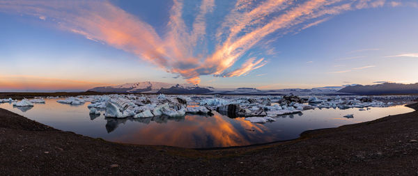 Panoramic view of icebergs in sea against snowcapped mountains and sky during sunset