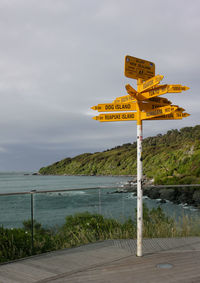 Sign on promenade with sea in background against cloudy sky