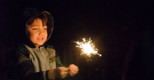 Close-up of cute boy holding sparkler at night