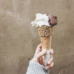 Cropped hand of woman holding ice cream cone against wall