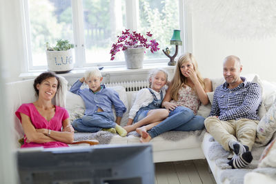 Family with three kids watching tv on sofa