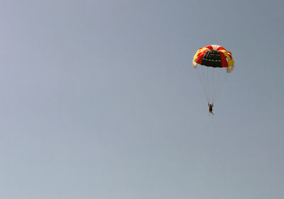 Low angle view of woman paragliding against clear sky