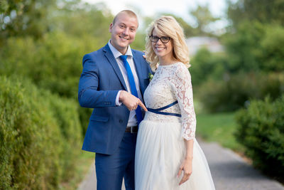 Portrait of smiling newlywed couple standing on footpath at park