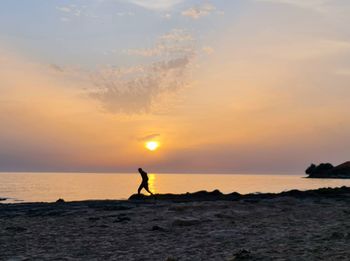 Silhouette person on sea against sky during sunset