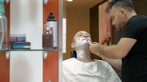 Barber doing shaving of mature man in salon