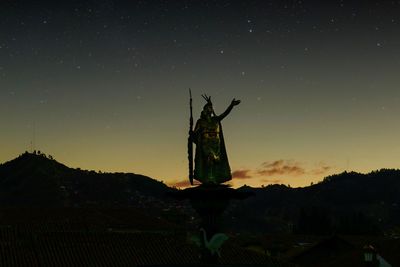 Silhouette cross on illuminated building against sky at night