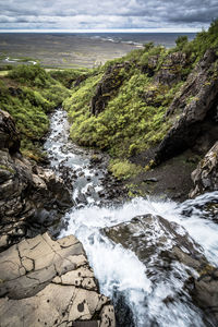 River flowing through rocks against cloudy sky