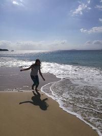 Girl walking on shore at beach against sky