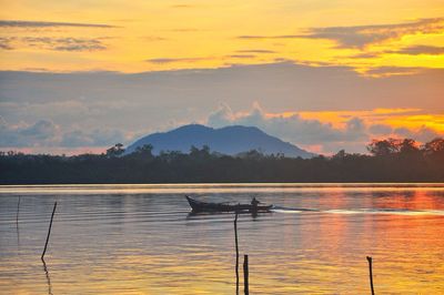 Mid distance of man rowing boat on sea against cloudy sky during sunset