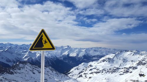 Road sign on snow covered mountain against sky