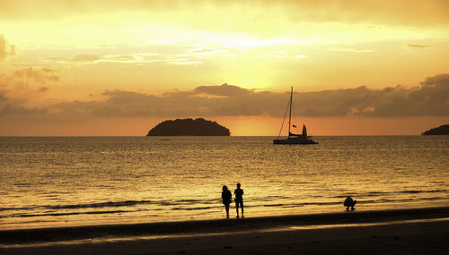 Silhouette people on beach against sky during sunset