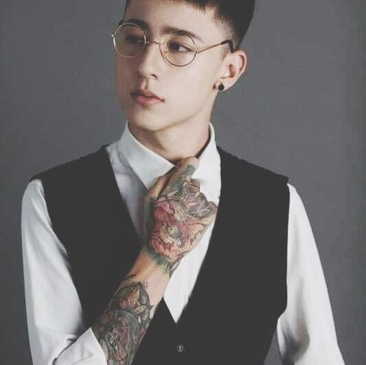 one person, portrait, adult, studio shot, young adult, indoors, tattoo, individuality, glasses, eyeglasses, men, headshot, fashion, person, looking at camera, eyewear, front view, formal wear, cool attitude, business, gray, serious, waist up, gray background, looking, hairstyle, human hair, clothing, creativity, vision care