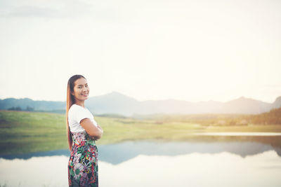 Portrait of smiling woman standing by lake against sky