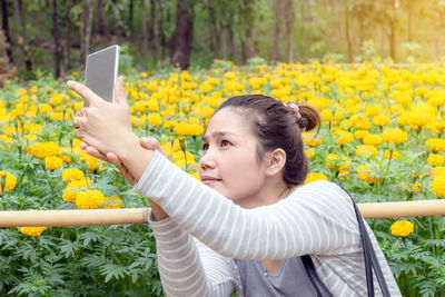 Asian woman using a smart phone to selfie with marigold fields.