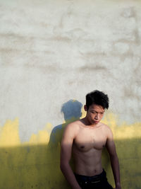 Shirtless young man standing against wall