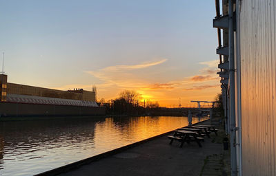 Bridge over river by buildings against sky during sunset