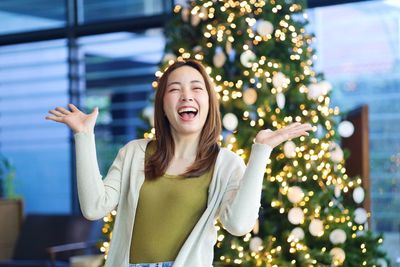 Portrait of young woman standing against illuminated christmas tree