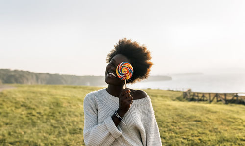 Young woman having covering eye with a lollipop, laughing