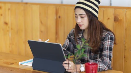 Young woman using digital tablet while sitting on table