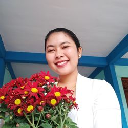 Low angle portrait of smiling woman with bouquet against ceiling