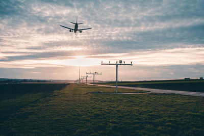 Airplane flying over land against sky during sunset