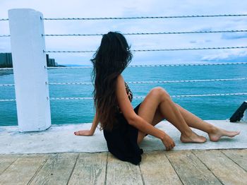 Rear view of woman sitting by sea against sky