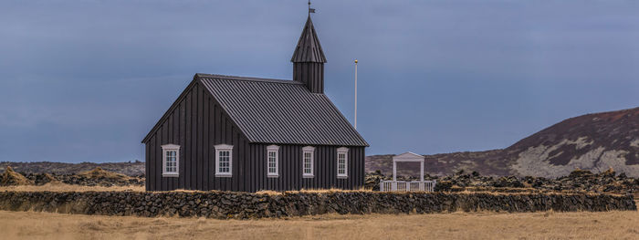 Panoramic view of black church of budir with rock wall surrounding it against a dark sky