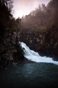 Scenic view of waterfall in forest against sky