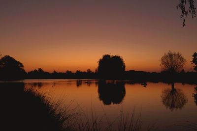 Silhouette trees by lake against sky during sunset