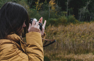 Side view of young woman taking photos of beautiful autumn nature with a vintage film camera