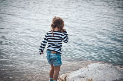 Rear view of boy standing on rock at sea