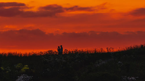 Silhouette man standing on field against orange sky