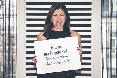 Young woman holding placard with message against wall