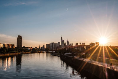 River by buildings against sky during sunset in city