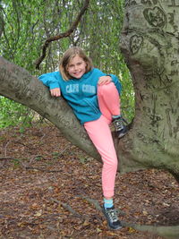 Full length portrait of happy girl sitting on tree trunk