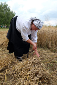 Rear view of woman with arms raised on field against sky