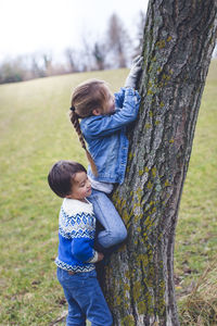 Girl with brother climbing tree on field