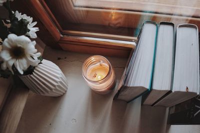 High angle view of flower vase by tea light candle and books on table at home