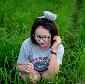 Woman wearing eyeglasses crouching on field against sky