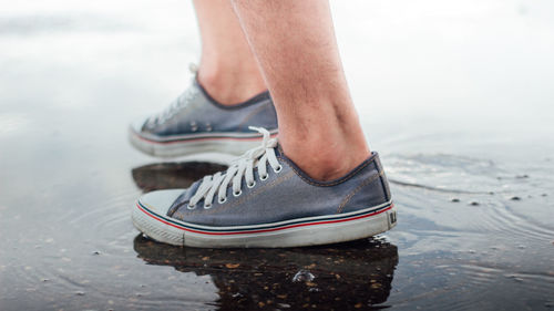 Low section of man wearing shoes while standing in water