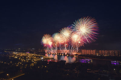 Firework display over illuminated city against sky at night