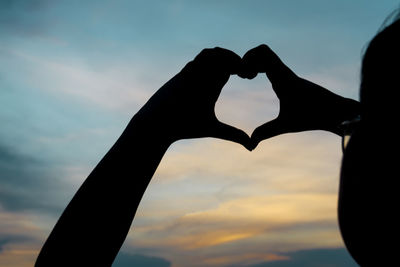 Close-up of hand holding heart shape against sky during sunset