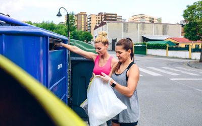 Female friends putting garbage in trash can in city