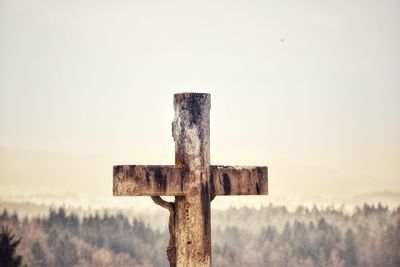 Close-up of cross on wooden post against clear sky