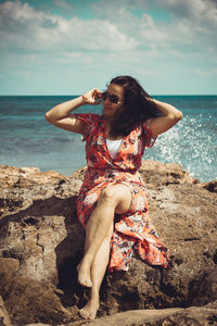 Full length of woman sitting on rock at beach